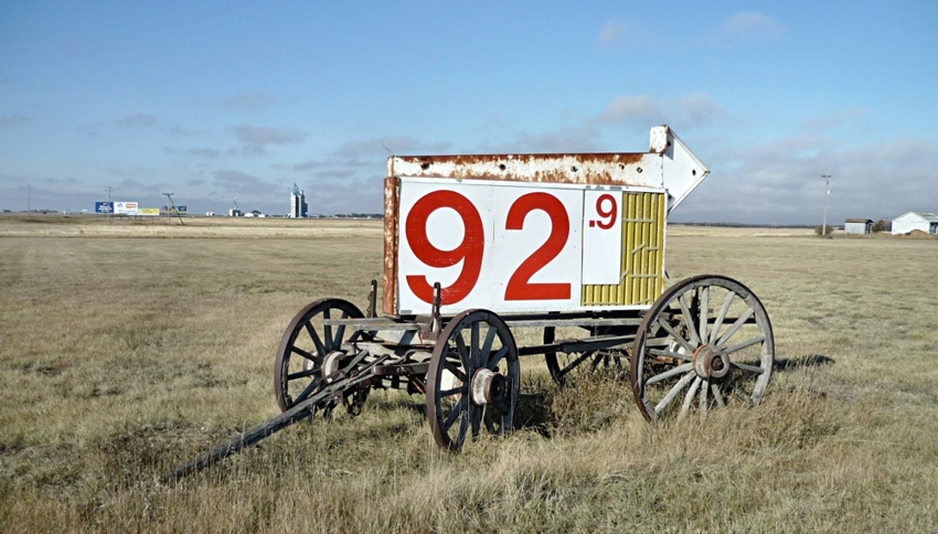  Large price sign with red letters and white arrows sitting on an old wagon in a field. The sign says "92.9." Photo by runrun